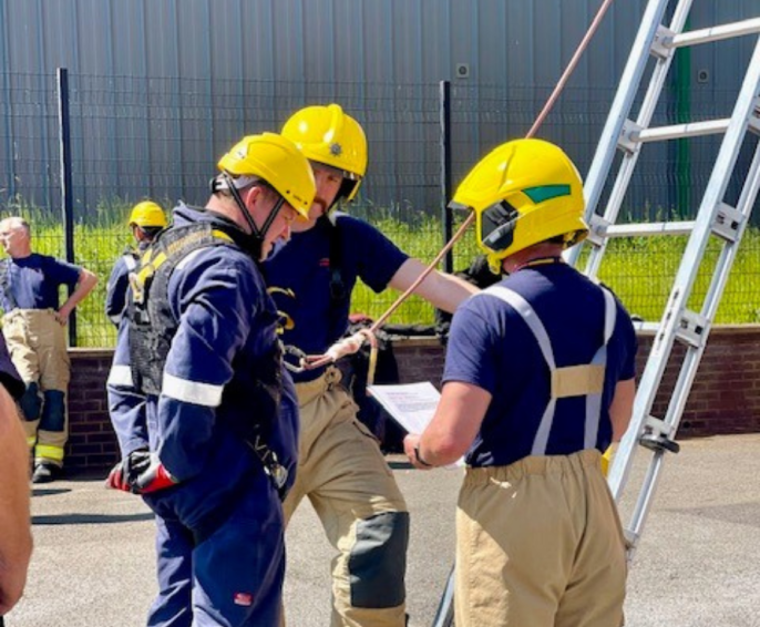 An On-Call assessment day with two male firefighters talking to a candidate in front of a tall ladder