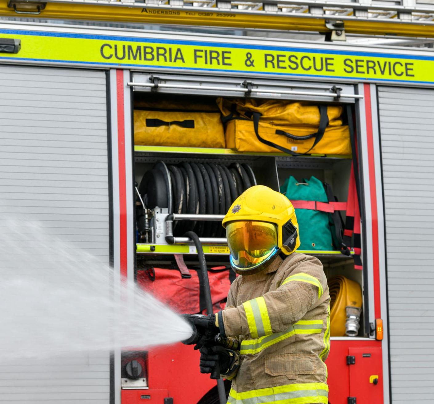 firefighter in PPE spraying water from a hose