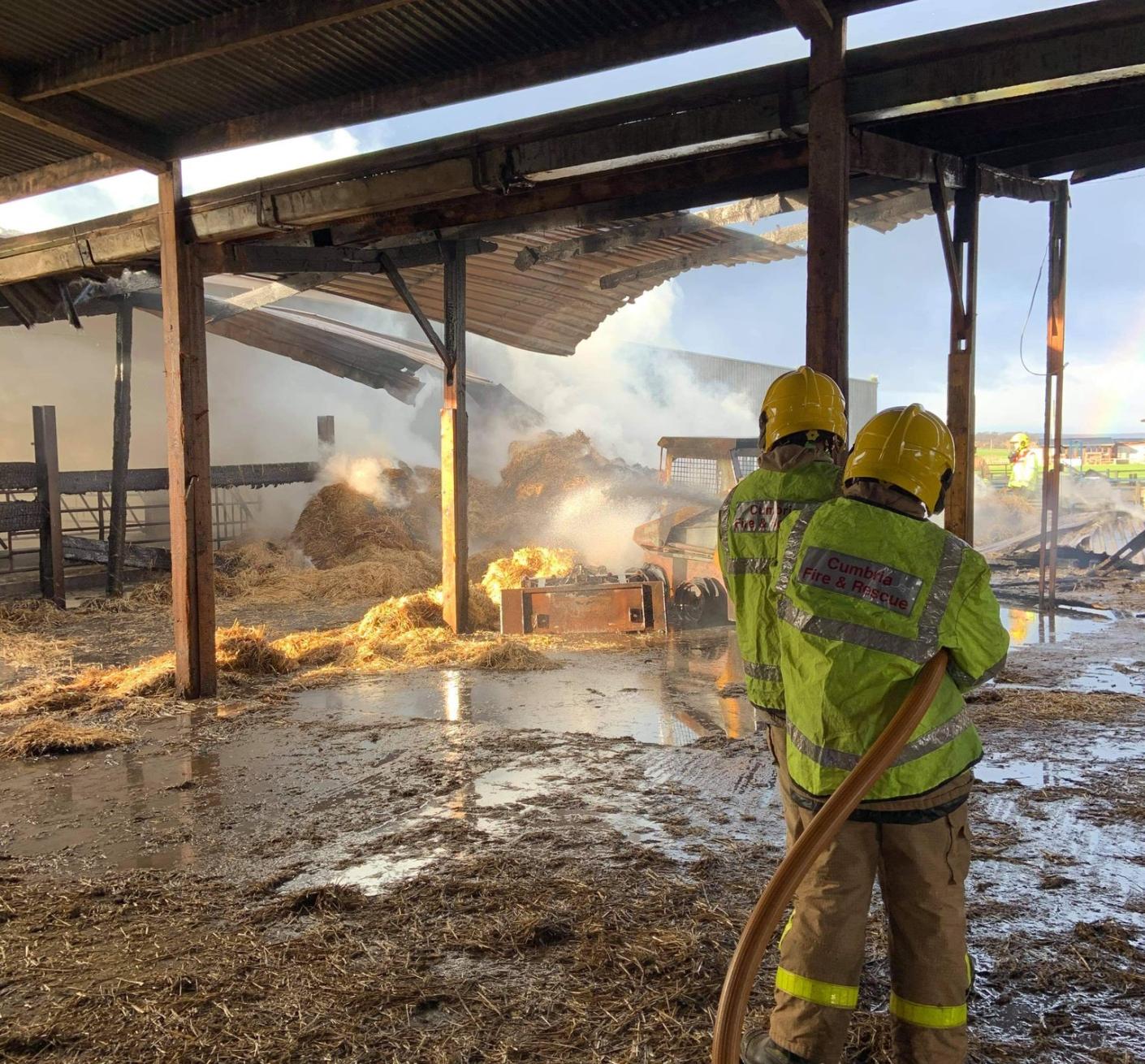 Two firefighters from Cumbria Fire and Rescue Service douse hay bales with water at a previous incident