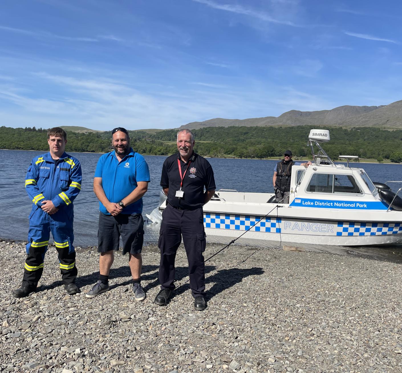 Three men stand together on the shore of one of the Lake District's waters