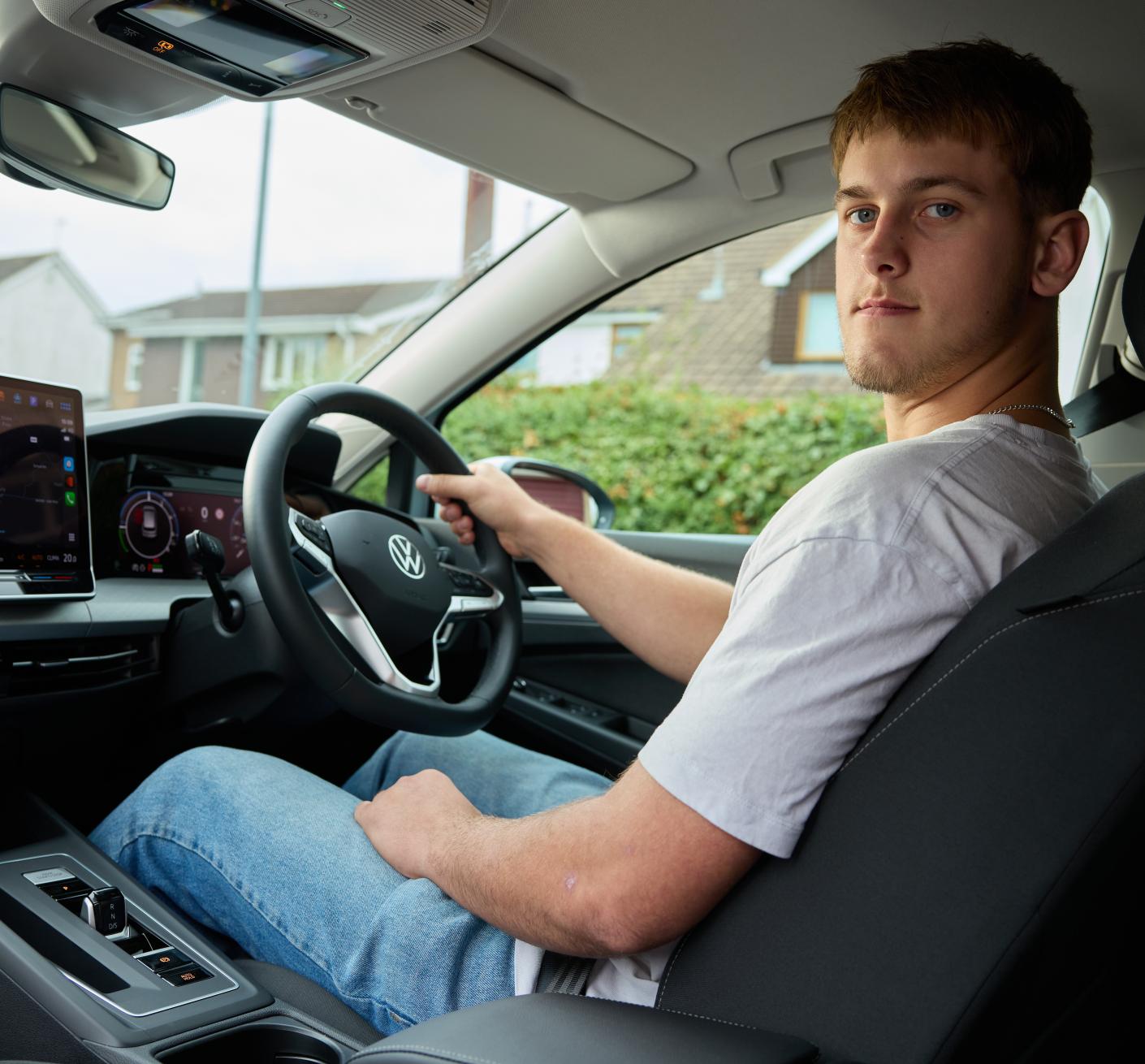 A person sitting in the driver's seat of a Volkswagen car, holding the steering wheel.