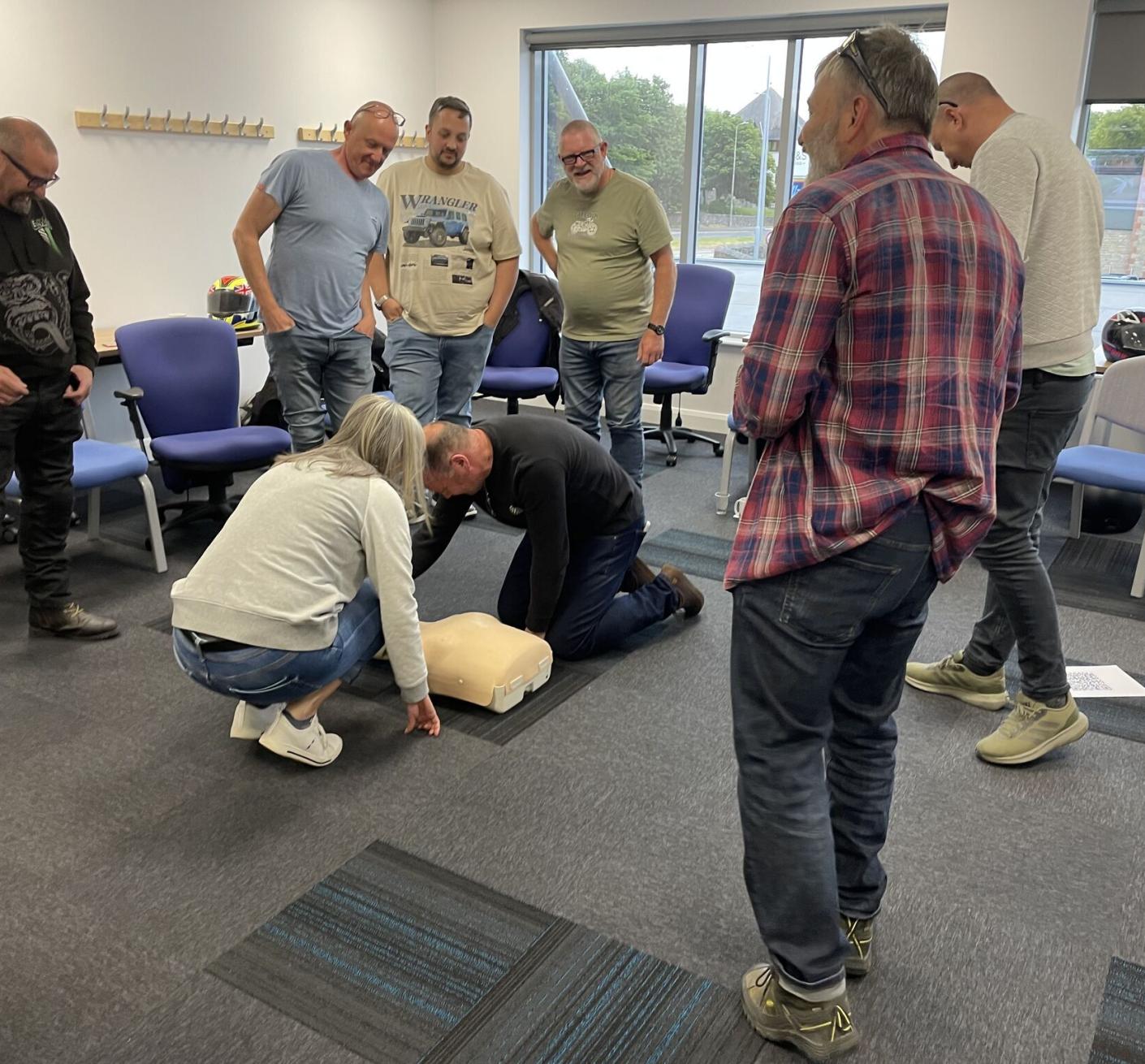 A man and woman crouch over a dummy