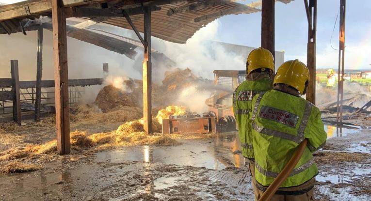 Two firefighters from Cumbria Fire and Rescue Service douse hay bales with water at a previous incident