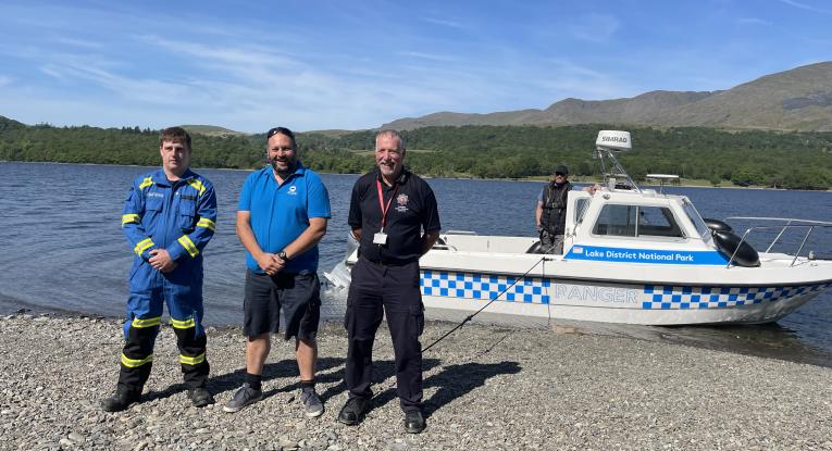 Three men stand together on the shore of one of the Lake District's waters