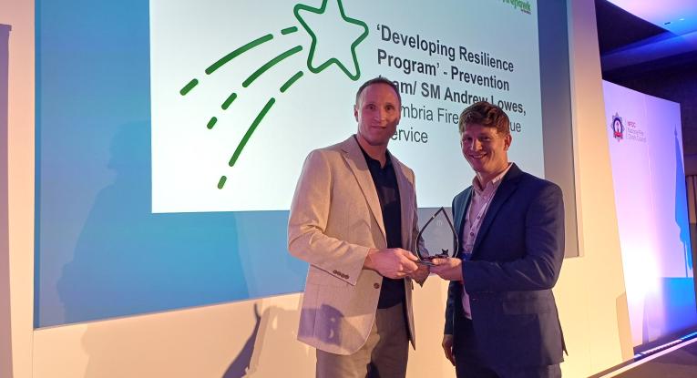 A firefighter is presented an award on stage