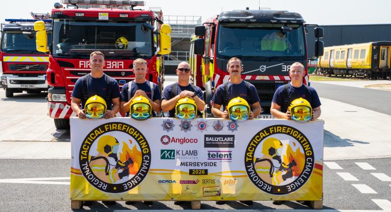 Five firefighters pose with their helmets in front of three fire engines
