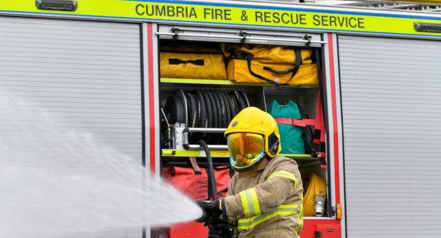 firefighter in PPE spraying water from a hose