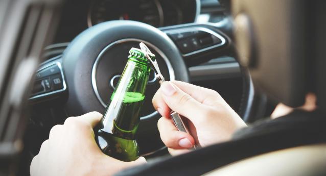 A man opens a bottle of beer behind the wheel
