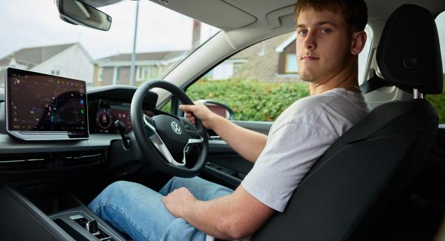A person sitting in the driver's seat of a Volkswagen car, holding the steering wheel.